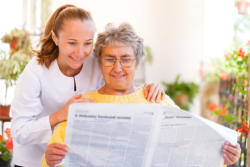 Senior reading a newspaper accompanied by a caregiver